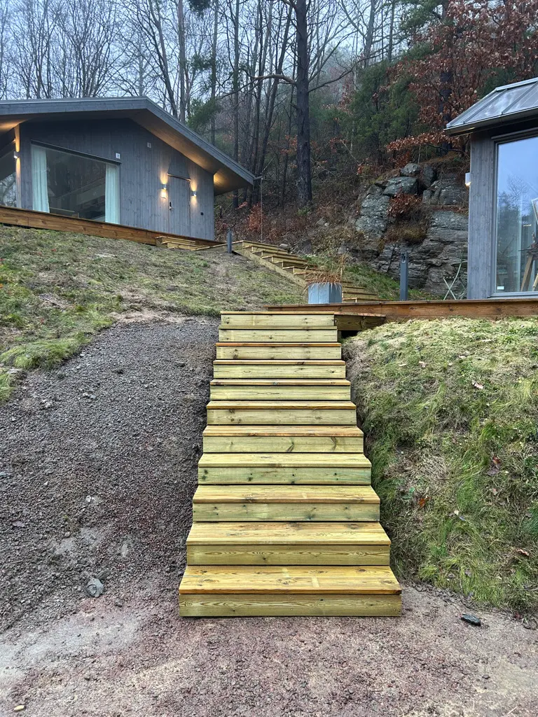 Nybyggd trätrappa i bergig tomt vid mörkt panelhus — KAAB Bygg