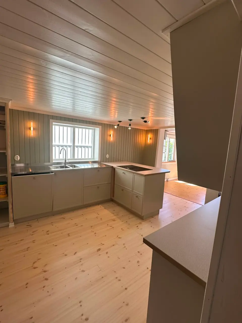 Vy från köket mot ett ljust rum med fönster och en kökshalvö under arbete